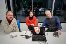 Die Mitglieder der Jury des Friedensfilmpreises 2022 sitzen an einem Tisch, ein Mitglied ist auf einem Laptop-Bildschirm zu sehen