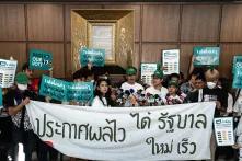 Menschen protestieren in einem Gebäude vor einer holzvertäfelten Wand, auf ihren Schildern steht auf Englisch und Thai: Protect our Vote