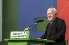 Werner Schulz, kurze weiße Haare und kurzer weißer Bart, steht in schwarzem Sakko hinter einem grünen Rednerpult. Auf dem Pult steht "Grün für ein besseres Europa"