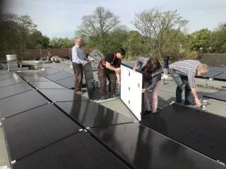 Vier Personen installieren ein Solaranlagenmodul auf einem Flachdach