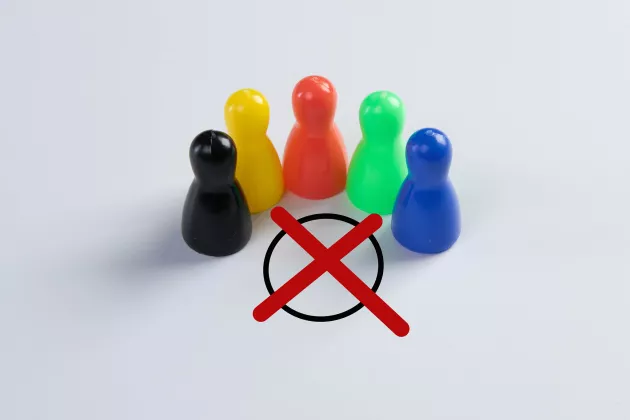 Fünf Spielfiguren in verschiedenen Farben stehen um einen aufgemalten Kreis mit einem roten Kreuz (wie auf einem Wahlzettel)