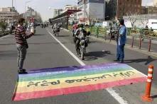 People on motorcycles are driving over a rainbowflag laying on the street