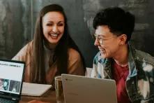 Zwei lachende junge Menschen vor einem Laptop