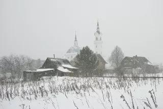 Russian village houses, barns and a church through a snow shower